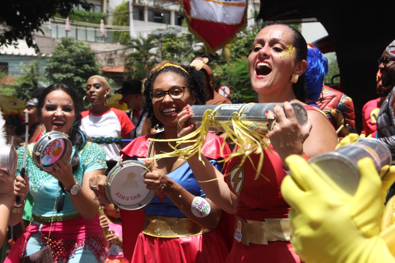 Meninas com equipamentos de música em mãos e vestimentas carnavalescas no meio da multidão 